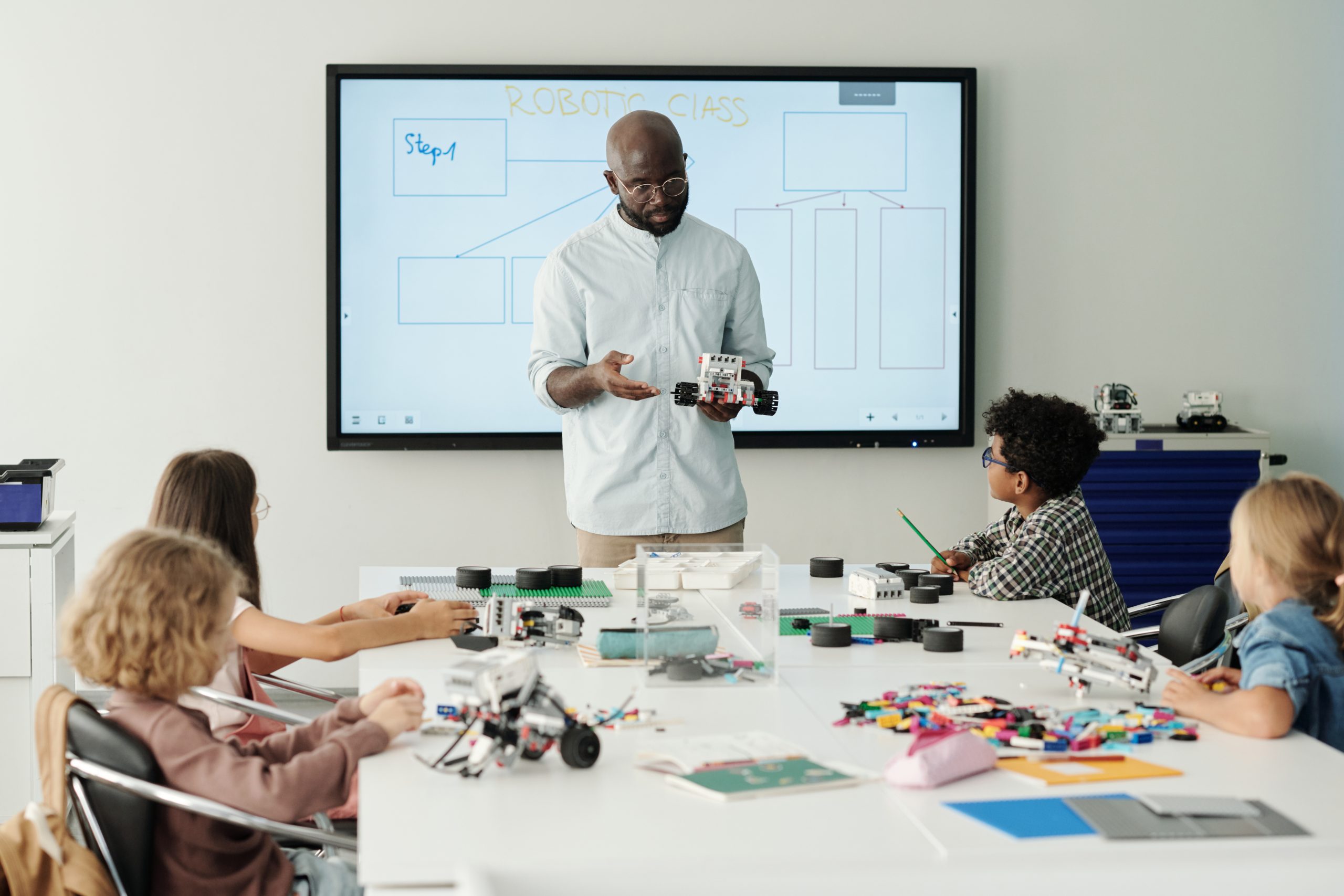 Confident male teacher explaining pupils how to connect parts of robot